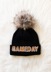 Flat lay of Panache Apparel’s black and tan Game Day winter hat featuring a folded cuff and faux fur pom.