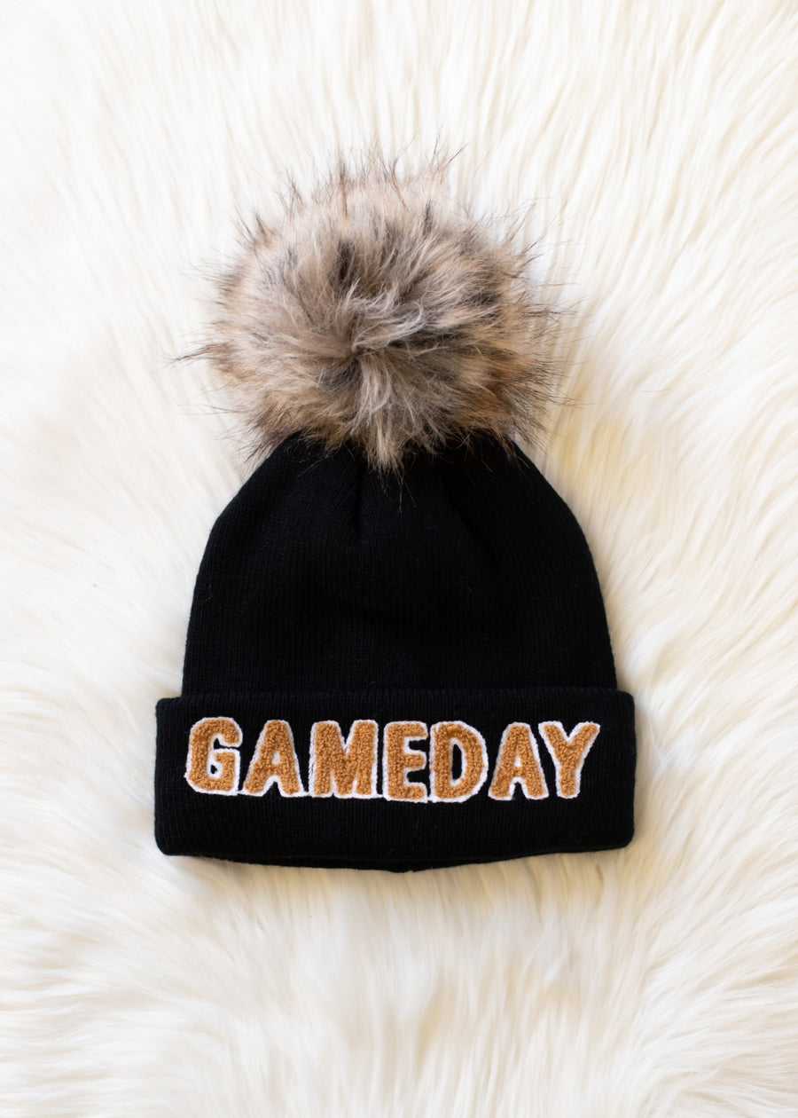 Flat lay of Panache Apparel’s black and tan Game Day winter hat featuring a folded cuff and faux fur pom.