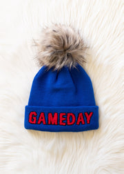 Flat lay of Panache Apparel’s royal blue Game Day pom hat featuring red lettering, a folded cuff, and faux fur detail.