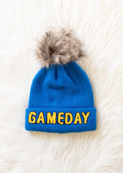 Flat lay of Panache Apparel’s blue and gold Game Day pom hat featuring bold lettering and a ribbed cuff.