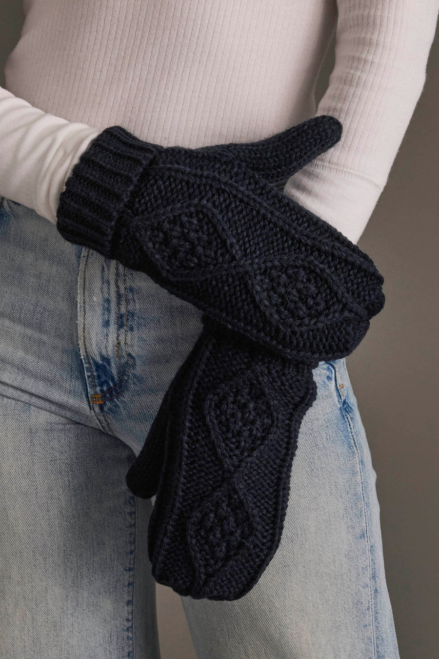 A person wearing light blue jeans, a white ribbed long-sleeve shirt, and holding the Panache Apparel Collection Navy Cable Knit Mittens.