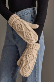 A person wearing a black long-sleeve shirt and blue jeans has their arms crossed, showing off the cozy Ivory Cable Knit Mittens from Panache Apparel Collection.