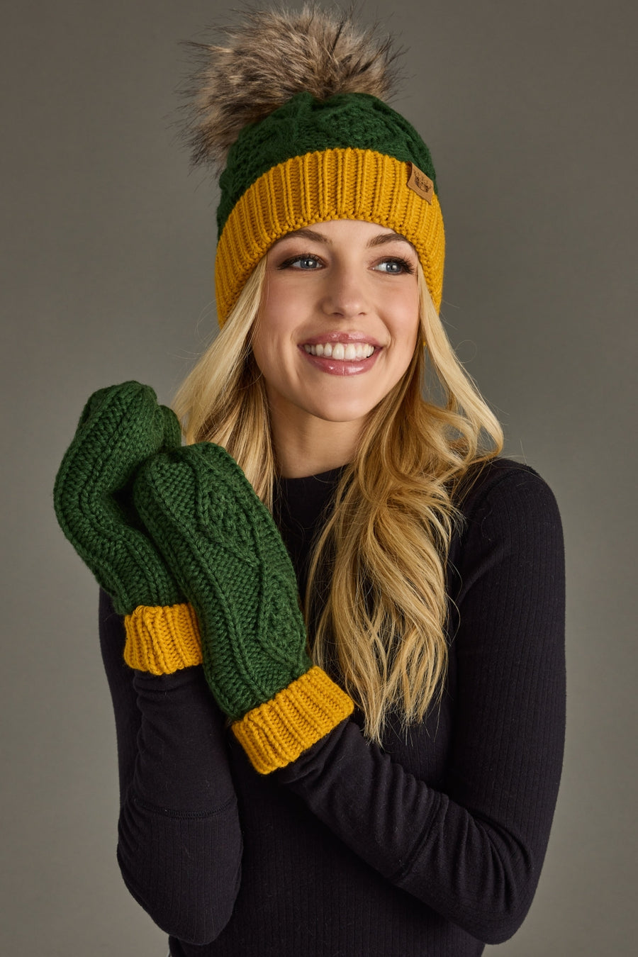 Woman wearing Panache Apparel’s green and gold cable knit mittens with matching pom hat.