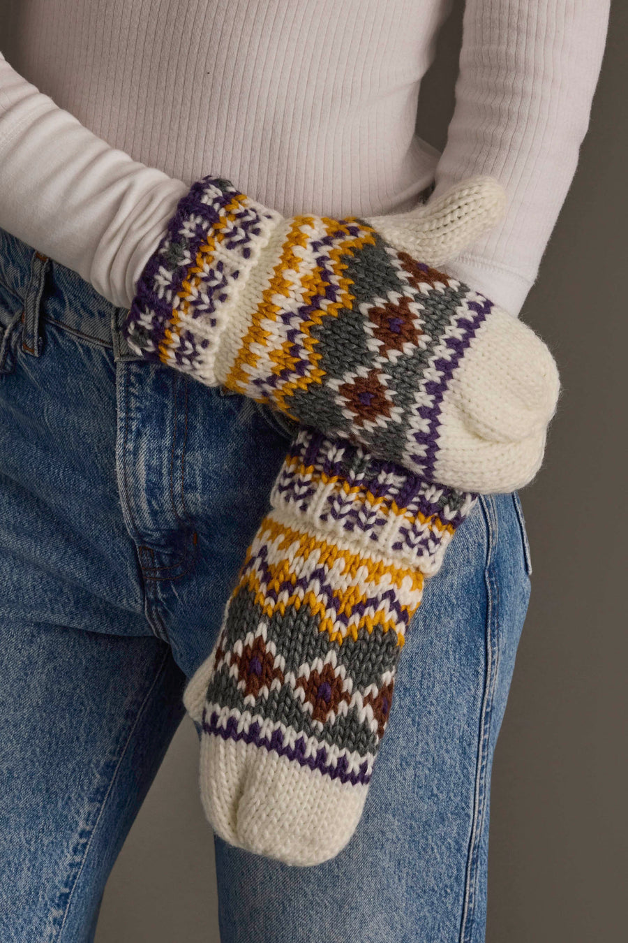 A person wearing blue jeans and a white ribbed shirt displays the Ivory, Purple & Gold Patterned Mittens from Panache Apparel Collection.