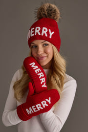A person wearing a Red Merry Knit Pom Hat and matching red mittens, both featuring the word MERRY in white letters.