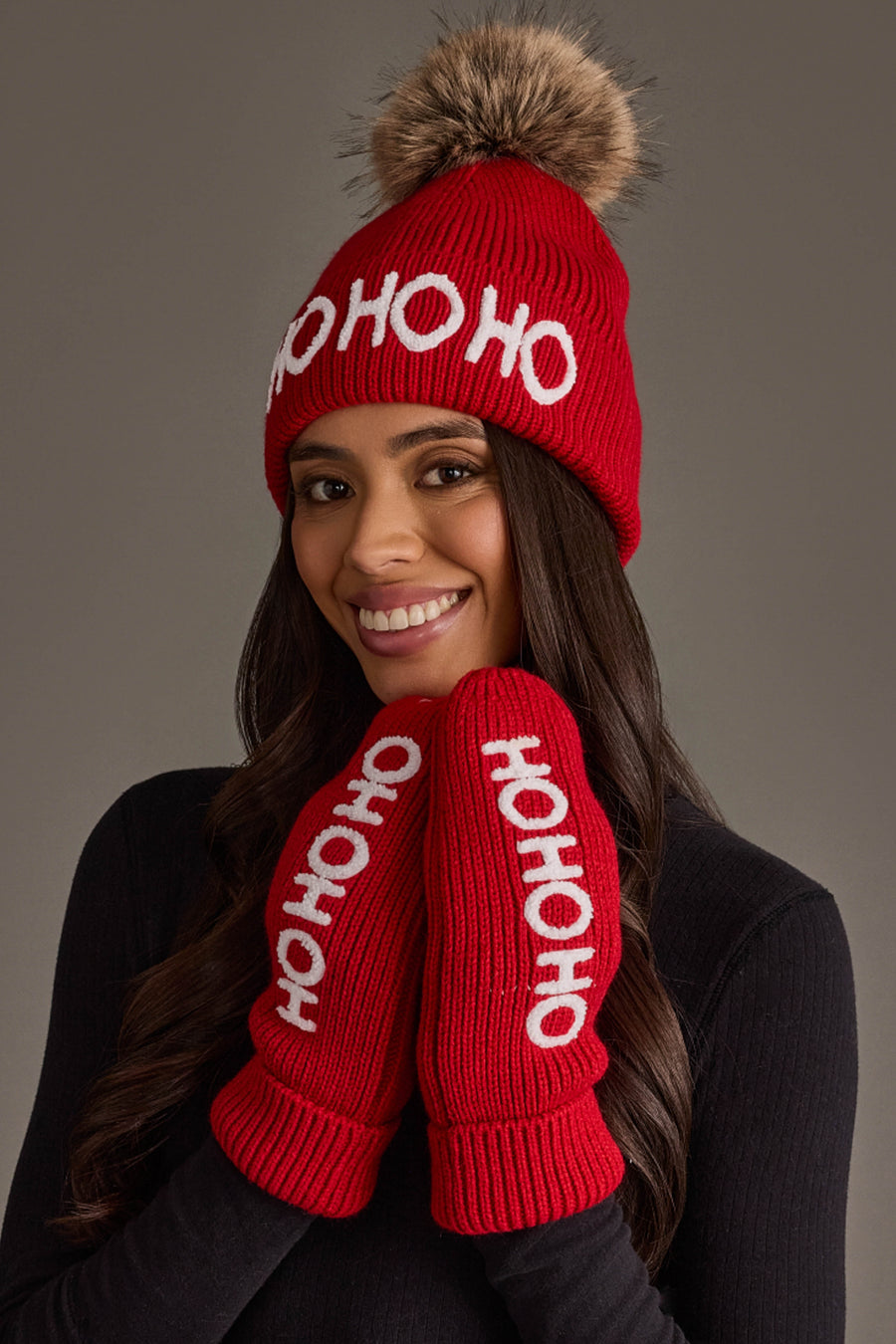 A person wears a Red Ho Ho Ho Knit Pom Hat with a faux fur pom-pom and matching mittens, both featuring the white text HO HO HO.