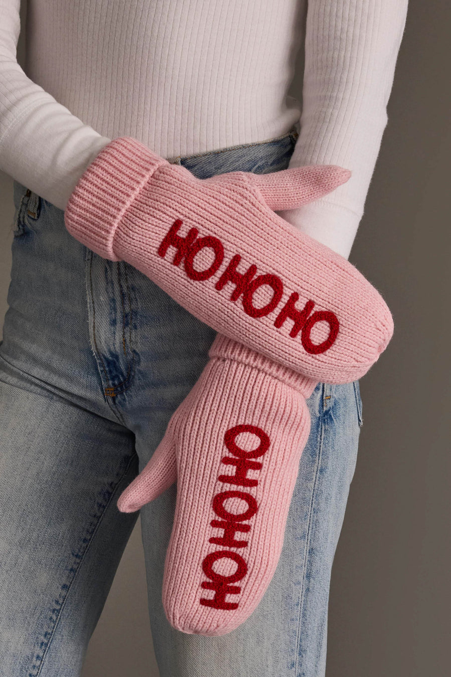 Pink Ho Ho Ho Knit Mittens from Panache Apparel Collection in pink fleece-lined knit with HO HO HO embroidered in red, worn over a white long-sleeve shirt and blue jeans.