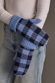 A person wearing light blue jeans, a white ribbed sweater, and the Panache Apparel Collection’s Light Blue & Navy Plaid Knit Mittens crosses their arms, prominently showcasing the mittens against a neutral background.
