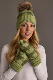 A woman with long blonde hair wears the Panache Apparel Collection Light Green & Olive Plaid Knit Pom Hat, featuring a faux fur pom-pom, and poses against a neutral background in a white ribbed top and coordinating green patterned mittens.
