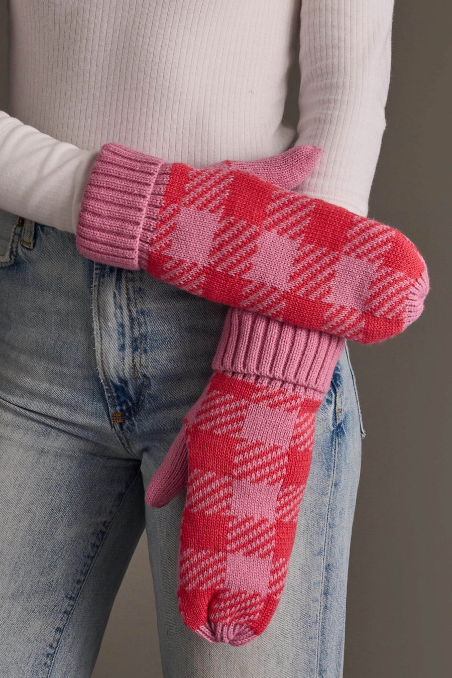 A person with arms crossed in front of their body is wearing Panache Apparel Collection’s Pink & Bright Pink Plaid Knit Mittens, a white ribbed long-sleeve top, and light-wash jeans.