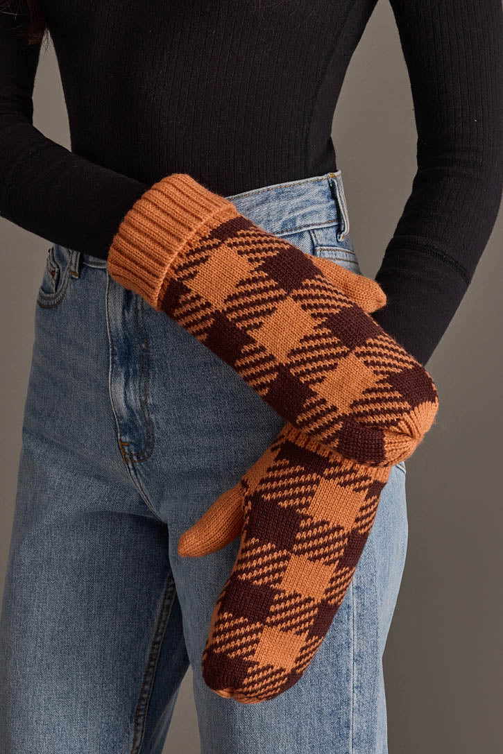 A person wearing high-waisted blue jeans, a black long-sleeve top, and Panache Apparel Collection’s Orange & Brown Plaid Knit Mittens, standing against a neutral background.
