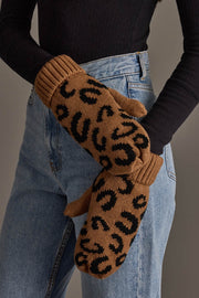 A person wearing blue jeans and a black ribbed top crosses their arms, displaying the Camel Leopard Pattern Knit Mittens from Panache Apparel Collection.