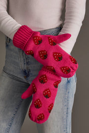 A person wearing the Panache Apparel Collection Strawberry Pattern Mittens, featuring a bright pink color with red strawberry designs, paired with a white ribbed sweater and blue jeans. Their arms are crossed against a plain, neutral background.