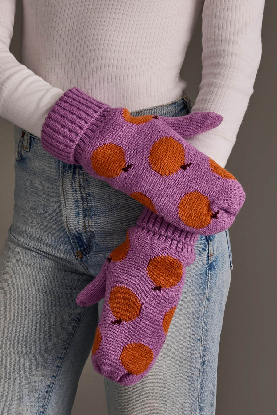 A person in a white ribbed shirt and blue jeans wears the Panache Apparel Collection Orange Pattern Knit Mittens.