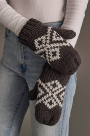 A person wearing light blue jeans and a white long-sleeve shirt is holding the Panache Apparel Collection Dark Gray & White Patterned Mittens.