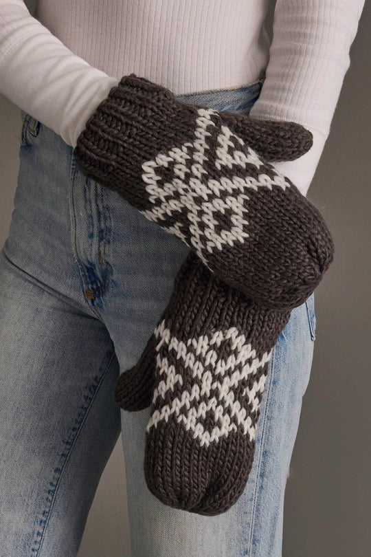 A person wearing light blue jeans and a white long-sleeve shirt is holding the Panache Apparel Collection Dark Gray & White Patterned Mittens.