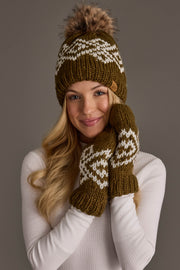 A woman smiles as she touches her cheek, wearing the Olive & White Patterned Pom Hat from Panache Apparel Collection and matching mittens. She has long blonde hair and is dressed in a white ribbed sweater.