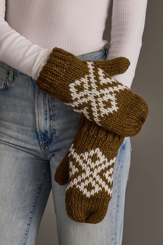 A person in a white long-sleeve shirt and blue jeans wears the Olive & White Patterned Mittens from Panache Apparel Collection.