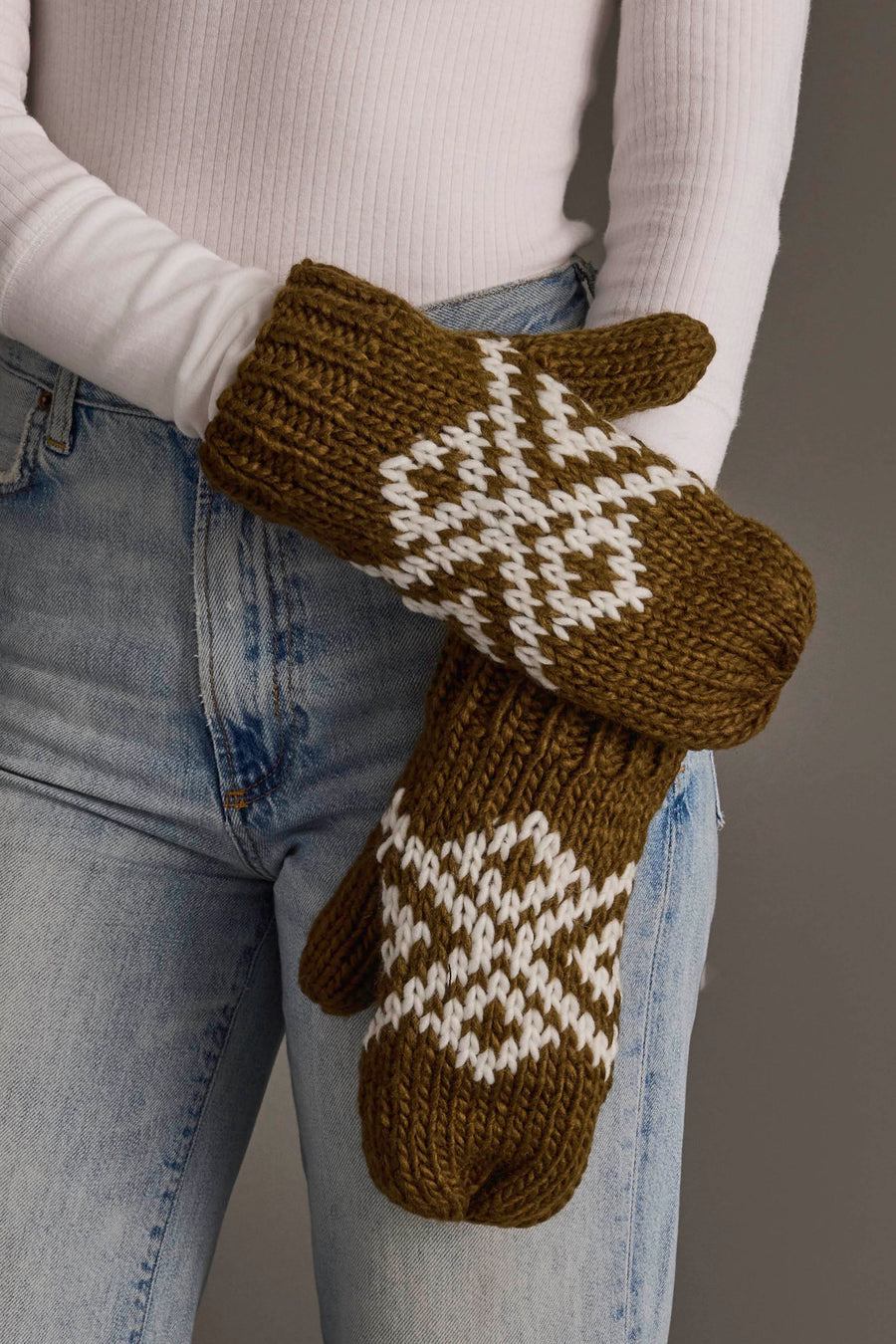 A person in a white long-sleeve shirt and blue jeans wears the Olive & White Patterned Mittens from Panache Apparel Collection.