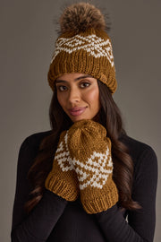 A woman wearing the Panache Apparel Collection Camel & White Patterned Pom Hat with matching mittens, paired with a black sweater, stands against a plain background.