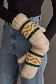 A person wearing blue jeans and a black long-sleeve top holds the Panache Apparel Collection Cream, Green & Gold Patterned Mittens.