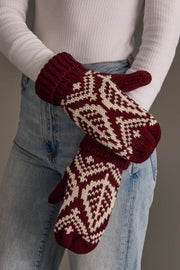 A person wearing a white ribbed sweater and blue jeans holds the Panache Apparel Collection Wine & Beige Patterned Knit Mittens, with the image focusing on the mittens and midsection rather than showing their face.