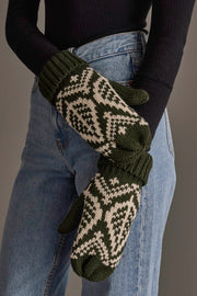 A person wearing blue jeans, a black long-sleeve top, and Panache Apparel Collection’s Olive & Beige Patterned Knit Mittens, standing with arms crossed in front of their body.