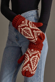 A person wearing blue jeans and a black sweater displays the Panache Apparel Collection’s Rust & Beige Patterned Knit Mittens.
