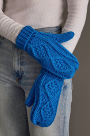 A person in light blue jeans and a white ribbed top holds the Panache Apparel Collection Blue Cable Knit Mittens.
