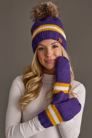 A woman in a white top wears the Panache Apparel Collection’s Purple, Gold & White Knit Pom Hat, paired with matching purple mittens featuring gold and white stripes, as she smiles softly in front of a plain background.