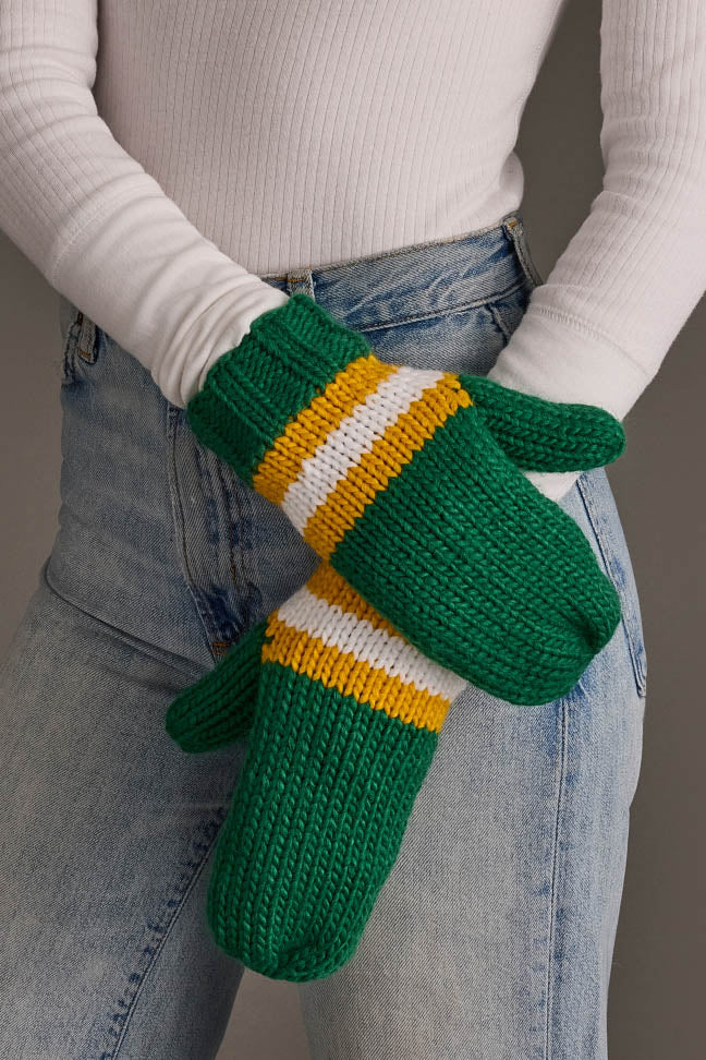 A person wearing a white ribbed shirt and blue jeans holds the Green, Gold & White Knit Mittens by Panache Apparel Collection.
