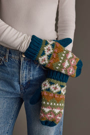 A person in a white long-sleeve shirt and blue jeans showcases the Panache Apparel Collection’s Blue, Green, Pink & Brown Patterned Mittens, chunky hand-knit mittens featuring a colorful fair isle design and ribbed cuffs.