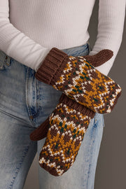 A person wearing blue jeans and a white ribbed shirt holds the Brown, Mustard & Cream Patterned Mittens from Panache Apparel Collection.