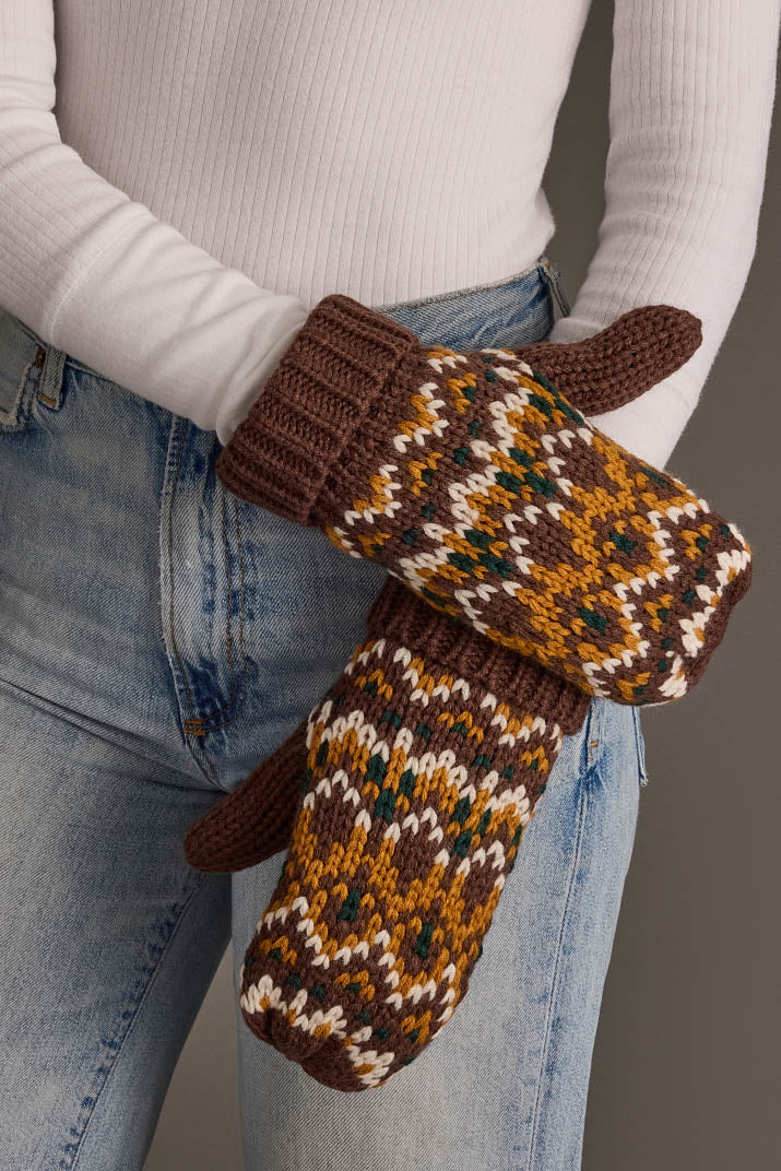 A person wearing blue jeans and a white ribbed shirt holds the Brown, Mustard & Cream Patterned Mittens from Panache Apparel Collection.