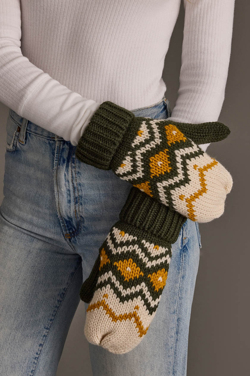 A person wearing a white ribbed sweater and blue jeans showcases the Olive, Cream & Mustard Patterned Mittens from Panache Apparel Collection.