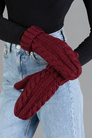 A person wearing a black long-sleeve top and blue jeans stands with arms crossed, showcasing the Burgundy Cable Knit Design Mittens from Panache Apparel Collection.
