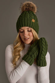 A woman wearing the Panache Apparel Collection’s Dark Green Cable Knit Design Pom Hat, paired with matching green mittens and a white sweater, poses against a neutral background.