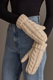 A person wearing a black ribbed long-sleeve shirt, blue jeans, and Panache Apparel Collection’s Cream Cable Knit Design Mittens stands against a plain backdrop.