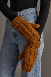 A person wearing a black long-sleeve shirt and blue jeans is shown with their hands crossed, wearing Panache Apparel Collection’s Mustard Cable Knit Design Mittens.