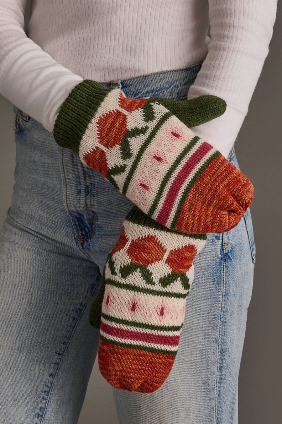 A person wearing blue jeans and a white ribbed sweater holds up their hands in Panache Apparel Collection’s Olive, Cream, Rust & Pink Patterned Mittens.