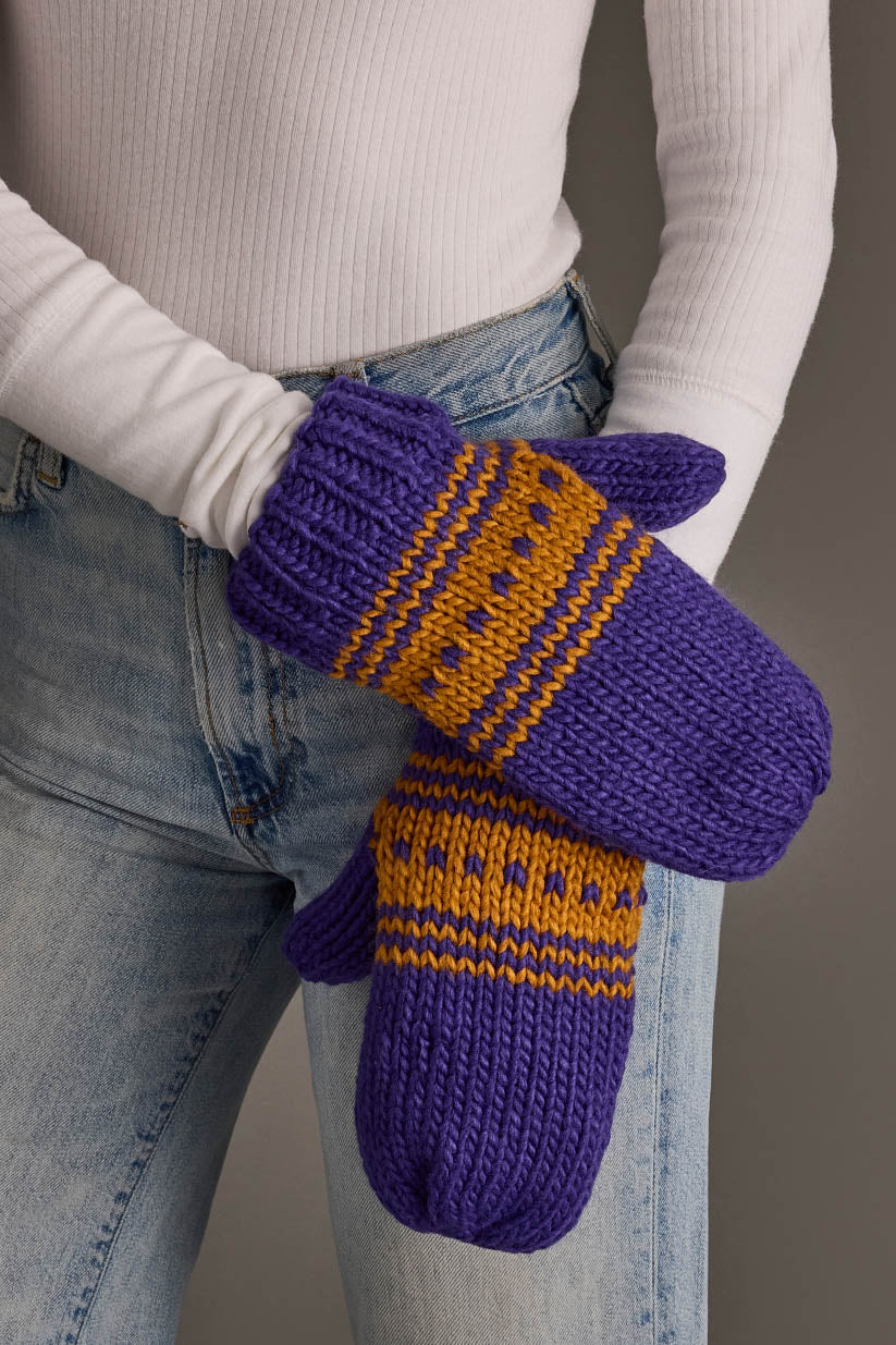 A person in blue jeans and a white ribbed top is wearing the Panache Apparel Collection Purple & Gold Patterned Knit Mittens.