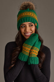 A woman in a black sweater smiles with her hands held to her face, wearing the Panache Apparel Collection's Green & Gold Patterned Knit Pom Hat and matching mittens against a plain background.