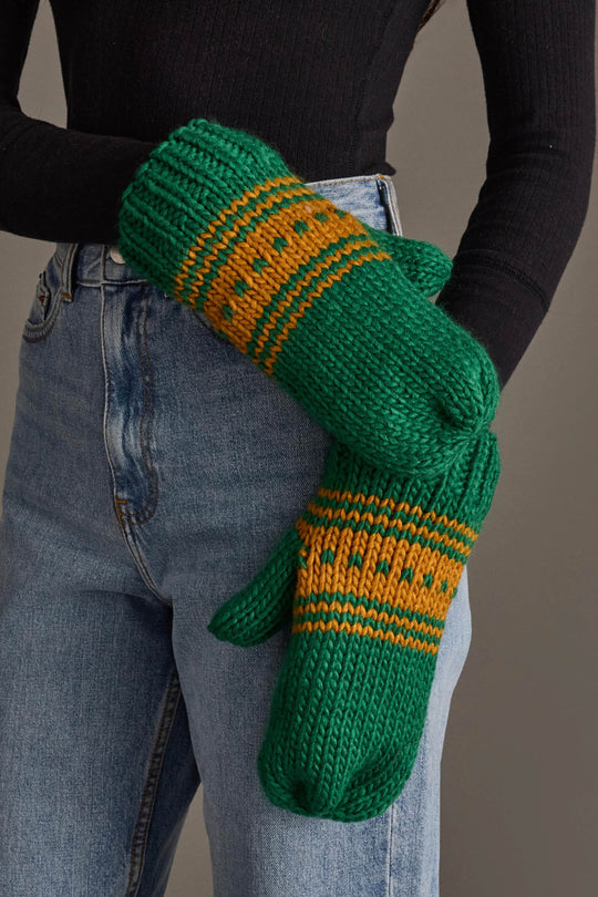 A person wearing blue jeans, a black long-sleeve top, and Panache Apparel Collection’s Green & Gold Patterned Knit Mittens stands against a neutral background.