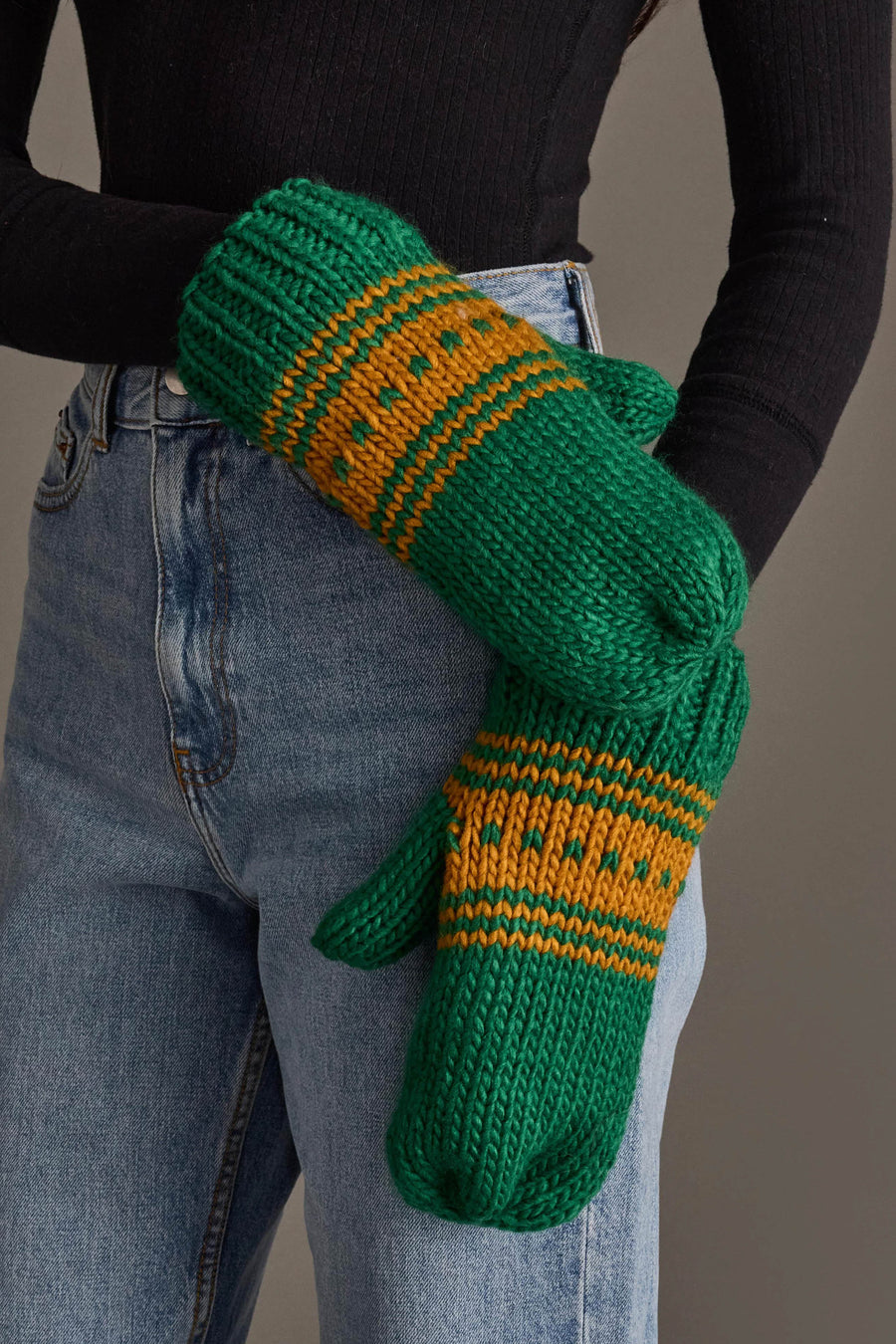 A person wearing blue jeans, a black long-sleeve top, and Panache Apparel Collection’s Green & Gold Patterned Knit Mittens stands against a neutral background.