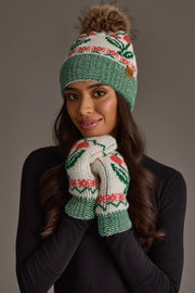 A woman with long, wavy hair smiles softly against a neutral background, wearing a green and white knit hat with a brown pom-pom and the Panache Apparel Collection Off White Cherry Pattern Mittens. The mittens feature red cherry designs that coordinate with her black top.