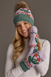 A smiling woman poses in front of a gray background wearing the Panache Apparel Collection Light Purple Cherry Pattern Pom Hat and matching mittens, paired with a white long-sleeve top.