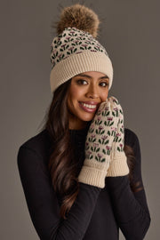 A smiling woman stands against a gray background wearing Panache Apparel Collection’s Cream Small Floral Pattern Knit Mittens and a beige knit hat with a pom-pom.