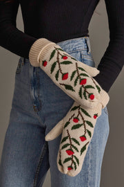 A person in blue jeans and a black ribbed sweater displays the Panache Apparel Collection Cream Floral Pattern Knit Mittens, featuring red berries and green leaves.