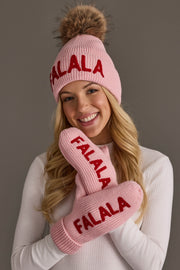 A woman wearing a pink knit beanie with a pom-pom and matching Pink Fa La La Knit Mittens, both featuring the red embroidered text FALALA.