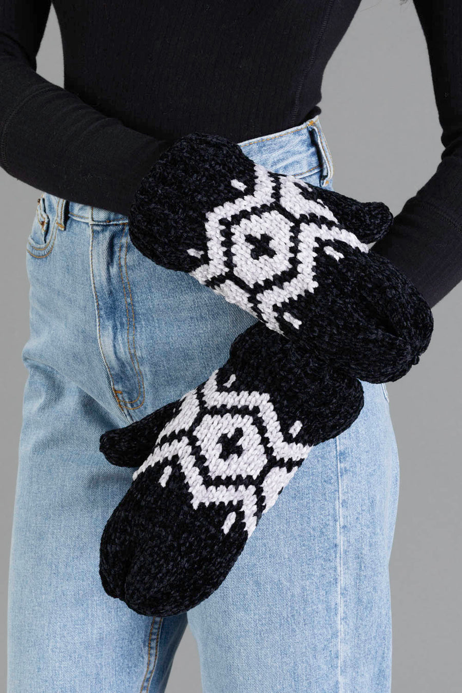 A person wearing blue jeans, a black long-sleeve shirt, and Panache Apparel Collection’s Black & Light Gray Patterned Chenille Mittens stands against a gray background.